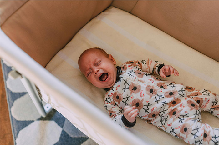 Crying baby in floral pajamas lying in crib, captured in a moment reflecting bizarre and paranormal experiences.
