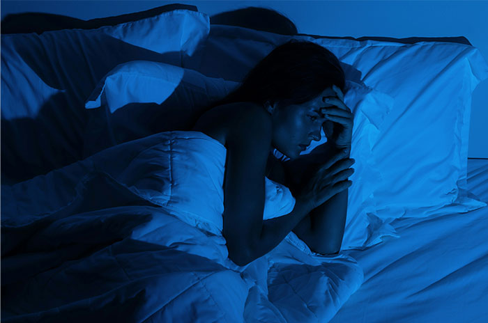 Woman lying awake in bed at night, troubled by bizarre and paranormal experiences she cannot explain.