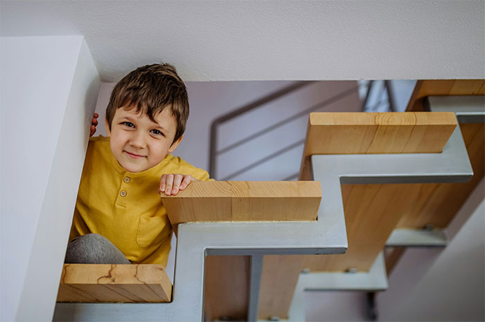 Young boy peeking through a modern wooden staircase, evoking curiosity about bizarre and paranormal experiences.