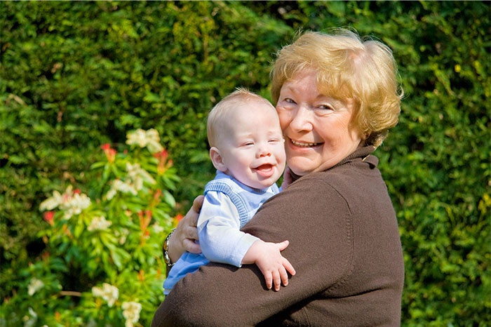 Elderly woman holding a smiling baby outdoors with greenery in the background, illustrating bizarre and paranormal experiences.