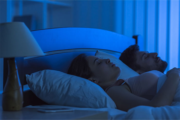 A couple lying awake in bed at night, experiencing bizarre and paranormal phenomena in a dimly lit bedroom.