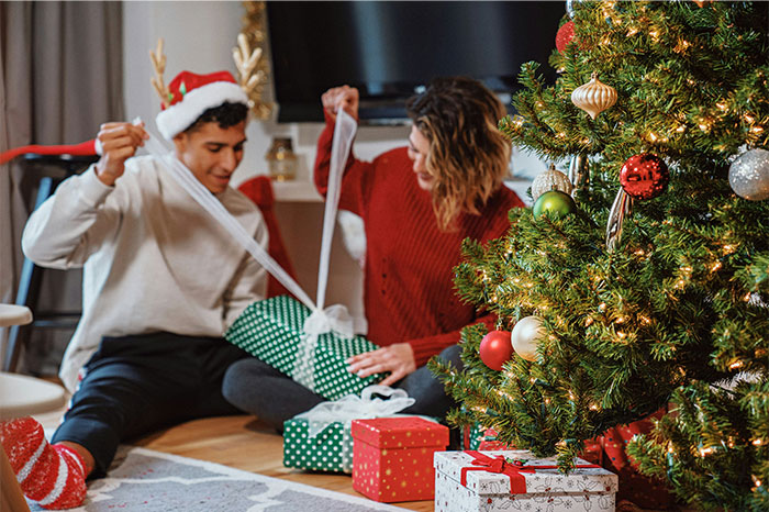 Couple unwrapping gifts by a Christmas tree, sharing a joyful moment capturing paranormal experiences atmosphere.
