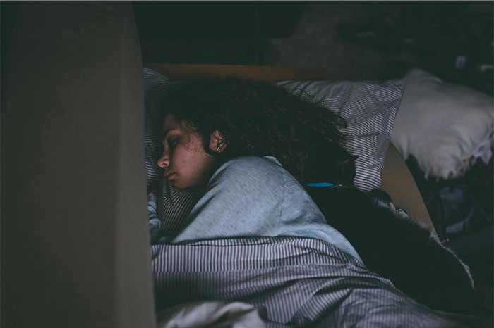 Woman sleeping peacefully on a bed at night, suggesting mysterious or paranormal experiences unseen around her.