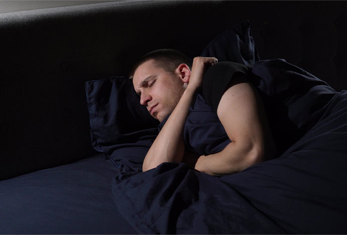 Man sleeping alone in dark room, possibly experiencing bizarre and paranormal sensations during rest or sleep paralysis.