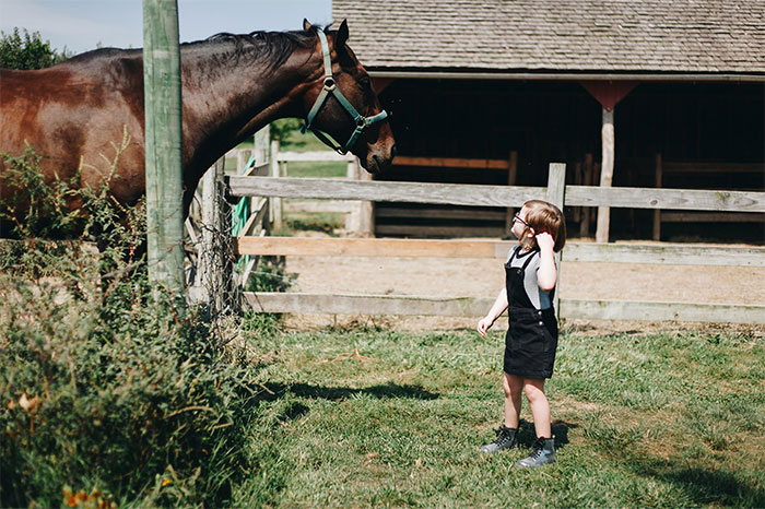 Young girl standing near a horse at a farm, capturing a bizarre and paranormal experience moment outdoors.