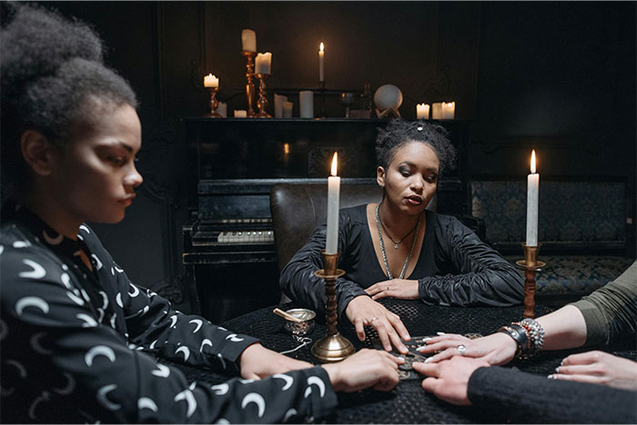 Three women engaging in a paranormal experience around a table with candles in a dark, mysterious setting.