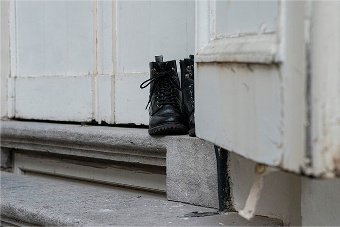 Black boots left abandoned on stone steps near an old door, evoking bizarre and paranormal experiences imagery.