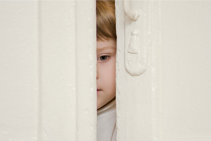 Child peeking through a narrow gap in a door, evoking a sense of bizarre and paranormal experiences mystery.