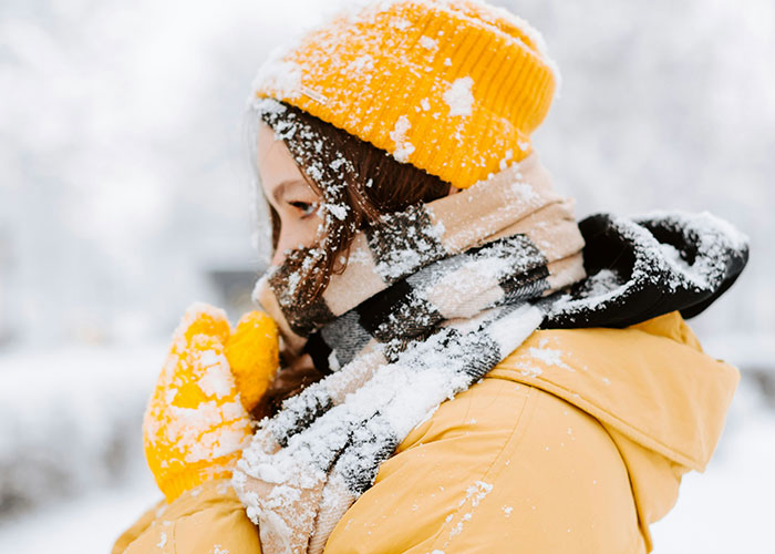 Person in yellow winter coat, hat, and gloves covered in snow, illustrating weird body quirks of the human body.