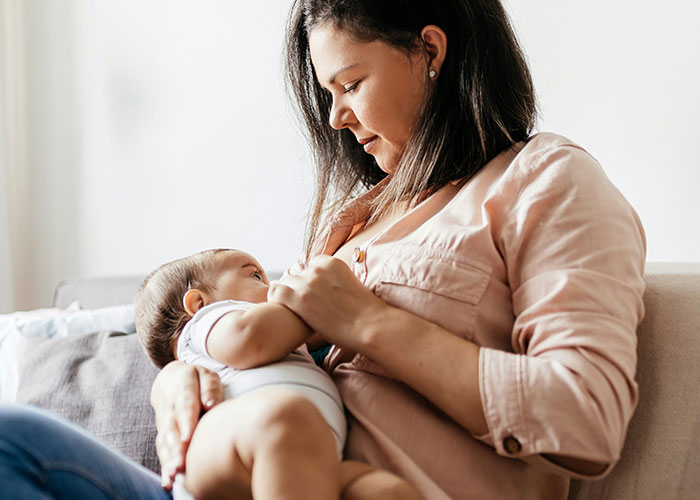 Mother breastfeeding baby on couch, illustrating fascinating weird body quirks related to the human body.