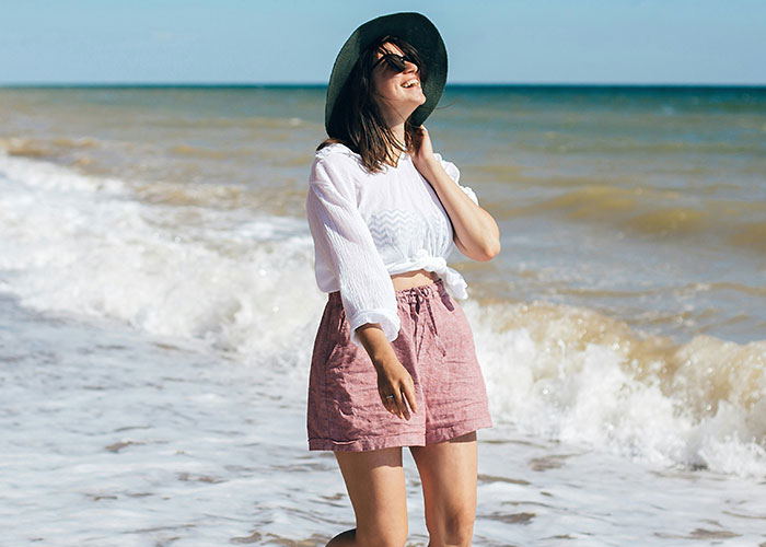 Woman wearing a hat and sunglasses smiling on the beach, illustrating weird body quirks of the human body.