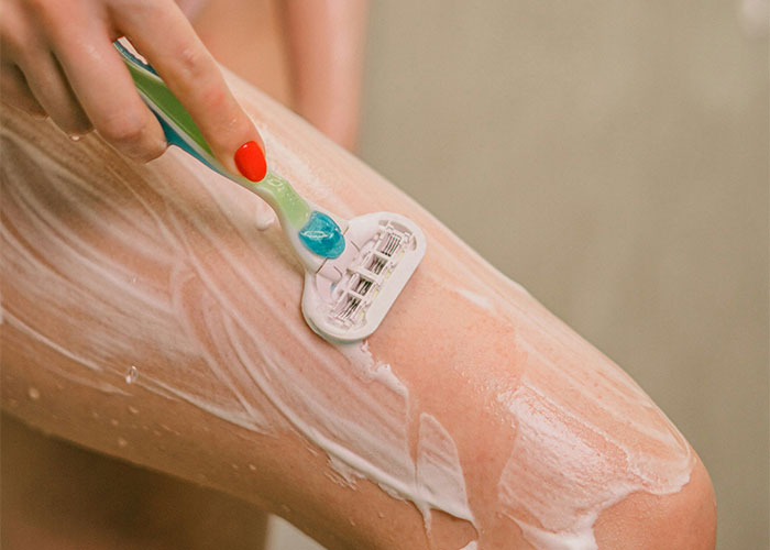 Close-up of a person shaving their leg with shaving cream, illustrating unique weird body quirks in human anatomy.