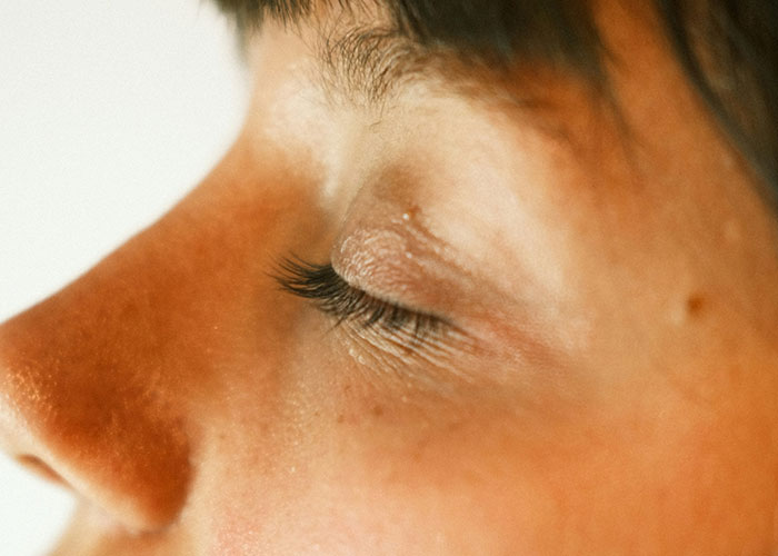 Close-up of a person’s face with closed eyes, illustrating weird body quirks of the human body.