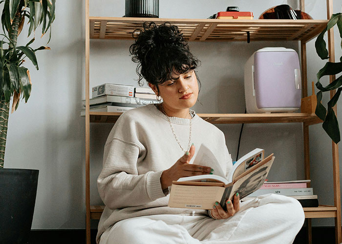 Young woman with curly hair reading a book indoors, illustrating weird body quirks and fascinating human body traits.