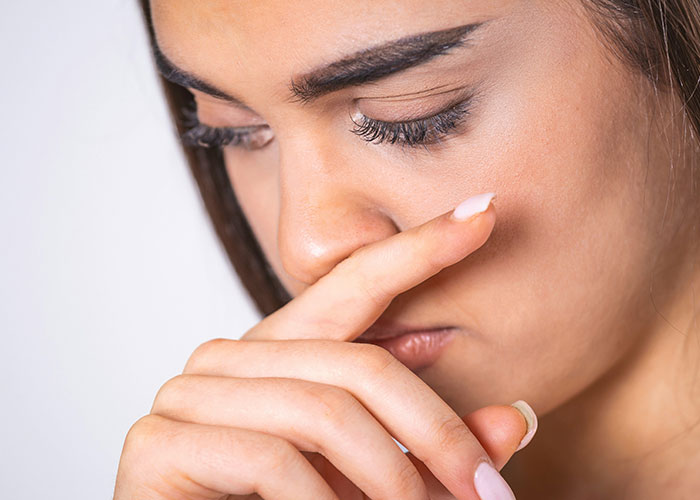 Close-up of a woman touching her nose, illustrating weird body quirks related to sneezing and human body reactions.