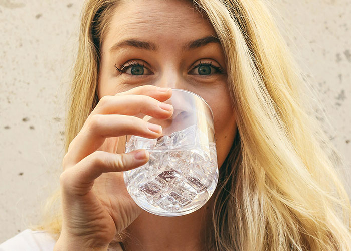 Woman with blonde hair drinking water from a glass, illustrating unique human body quirks and fascinating physical reactions.