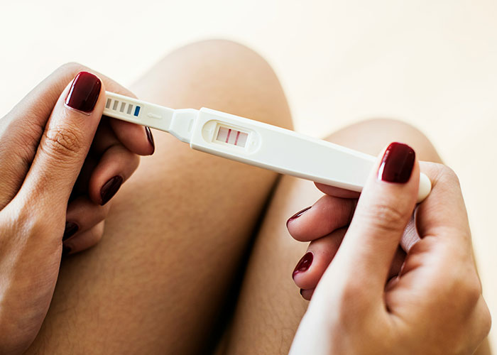 Hands with dark red nail polish holding a positive pregnancy test, illustrating weird body quirks and human body fascination.