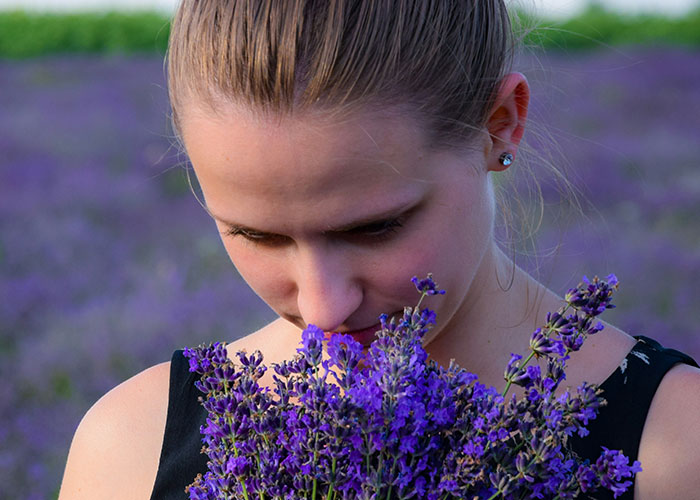 Young woman smelling fresh lavender flowers in a field, illustrating weird body quirks and fascinating human body traits.