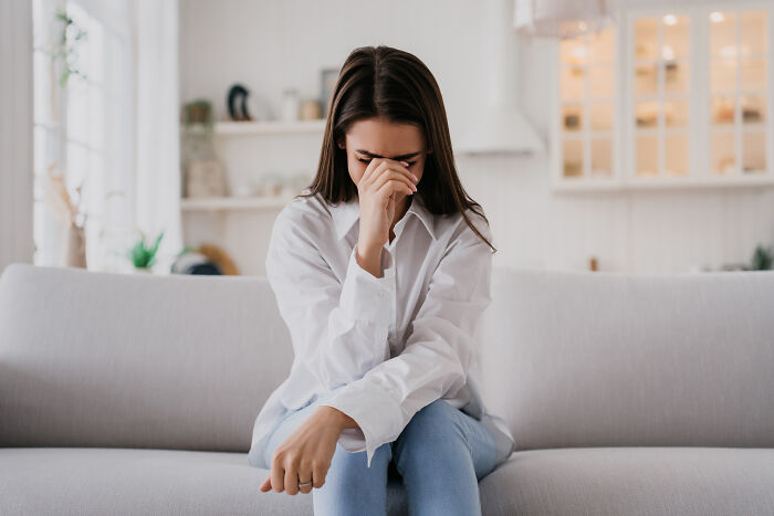 Young woman sitting on a couch with a stressed expression, reflecting on things people would never admit in real life.