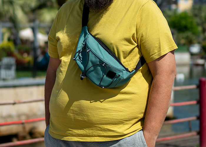 Man wearing a yellow t-shirt and teal bag standing outdoors near water, representing vacation trips gone wrong.