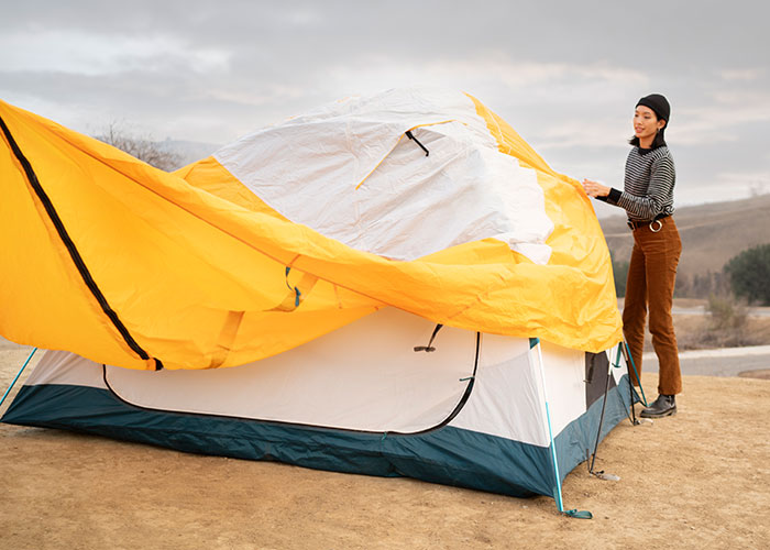 Woman setting up a yellow and white tent outdoors during a cloudy day on a camping trip gone wrong vacation.