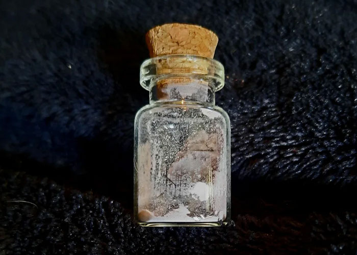 Small glass vial with cork stopper, containing white powder, sitting on a textured dark fabric background, vacation nightmares concept.
