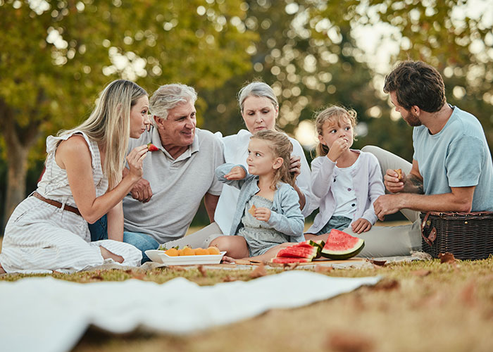 Family enjoying a picnic outdoors with watermelon and snacks, highlighting vacations that ended up being trips to hell.