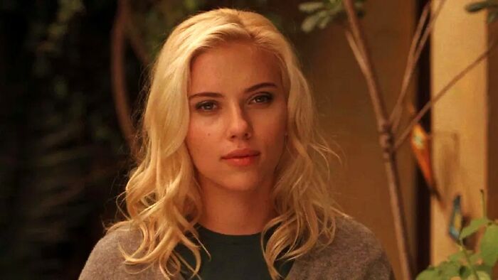 Woman with blonde hair and neutral expression sitting indoors near plants, illustrating meeting an idol experience.