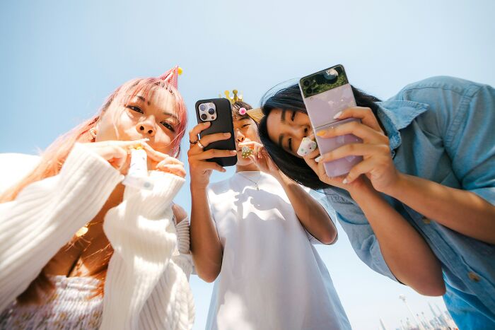 Three young women wearing party hats using smartphones outdoors, highlighting popular overhyped products in use.