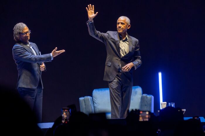 Barack Obama waving to audience on stage during event, discussing life with wife Michelle after presidency. Barack Obama waving to audience on stage during event, discussing life with wife Michelle after presidency.
