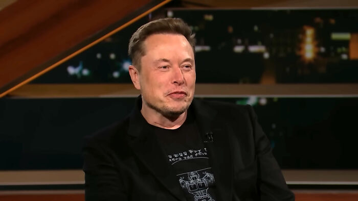 A man in a black blazer and graphic t-shirt speaking on a dark set about real-life stories of people changing.