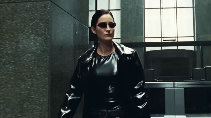 Female character in black leather outfit and sunglasses walking confidently in a modern building, portraying well-written female characters.