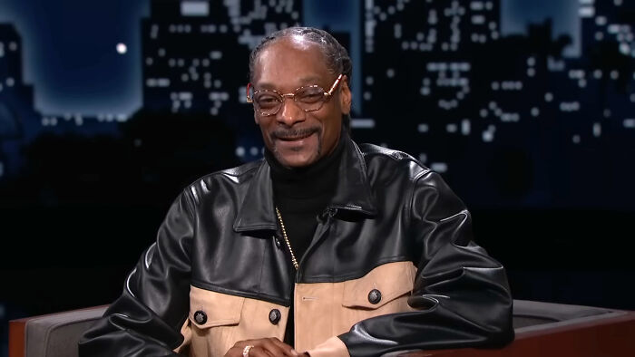 Man wearing glasses and a black and beige leather jacket smiling during a discussion about real-life stories of change.