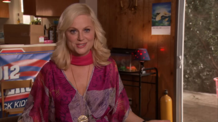 Blonde woman in a colorful blouse speaking in a cozy wooden room, representing well-written female characters in movies.
