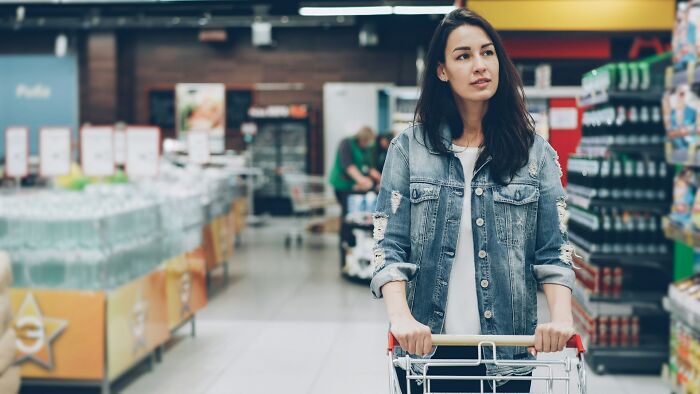 Young woman pushing a shopping cart in a grocery store aisle, illustrating unexpected and fast ways people get fired.