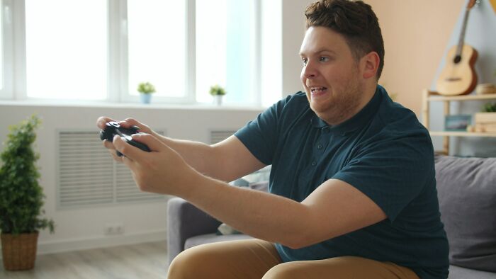 Adult man playing video games intensely at home, showing a playful side of adults who failed to grow up.