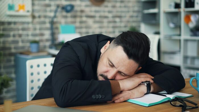 Man in black blazer sleeping at desk with notebook and eyeglasses, illustrating fastest ways people get fired.