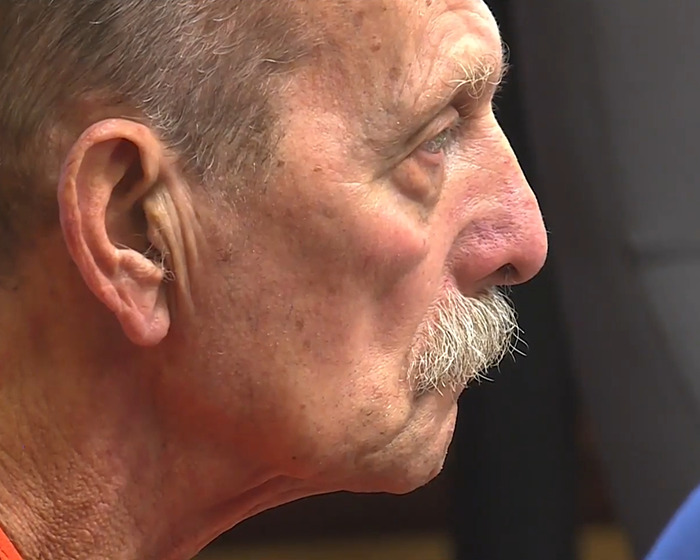 Elderly man with mustache in profile, reflecting on teen chewed through ropes escape survival story in podcast.