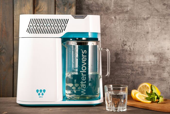 Water dispenser with glass pitcher and glass of water on wooden surface, highlighting product sabotage by companies.