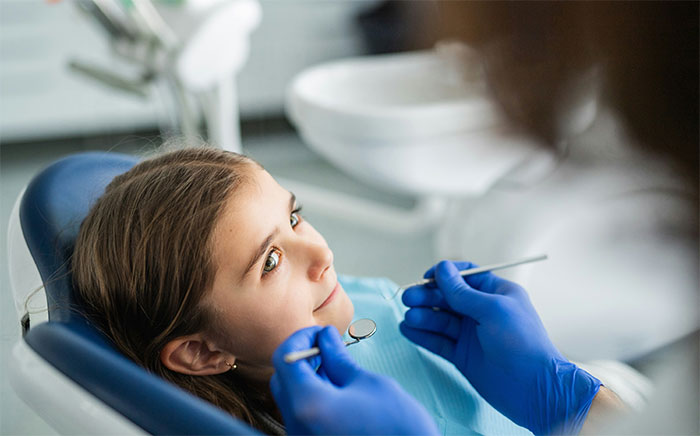 Young patient in dental chair being examined by dentist wearing blue gloves during a medical checkup.