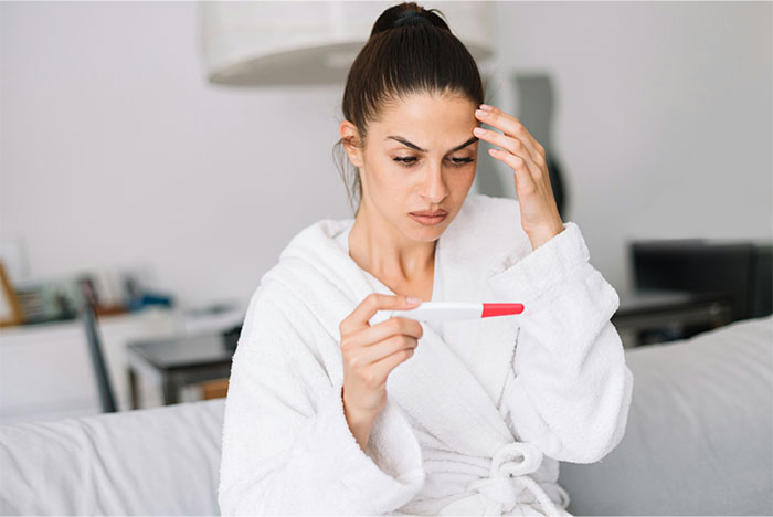 Woman in a white robe looking concerned at a pregnancy test, illustrating patients trying to fool doctors with lies.