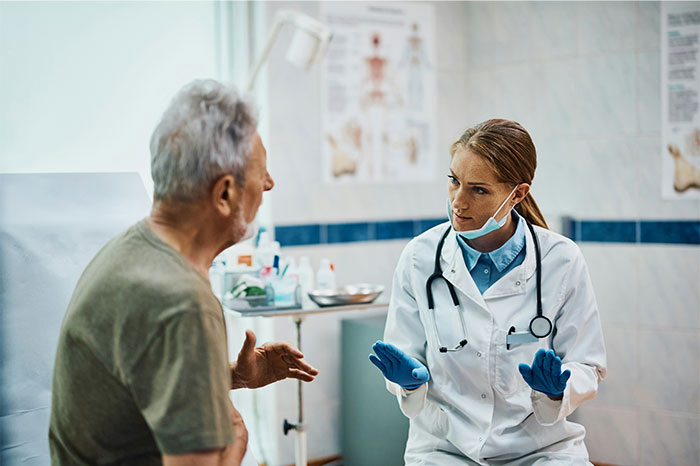 Doctor wearing gloves and mask talks to elderly patient in clinic, highlighting patients trying to fool doctors with lies.