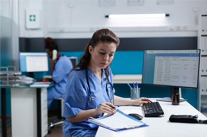 Female doctor reviewing patient files at desk with computer, illustrating patients trying to fool doctors with ridiculous lies.