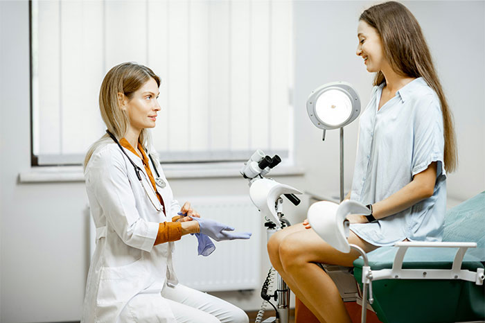 Female doctor putting on gloves while talking to a patient during a medical examination in a clinic setting
