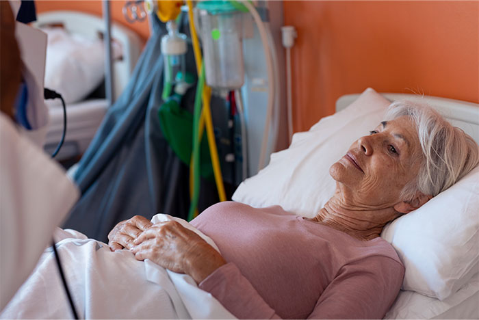 Elderly woman lying in hospital bed, appearing thoughtful as medical staff attend, illustrating patients trying to fool doctors.