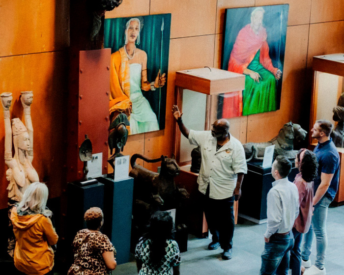 Visitors listening to a guide explaining exhibits during an African-American museum visit with cultural artworks displayed.