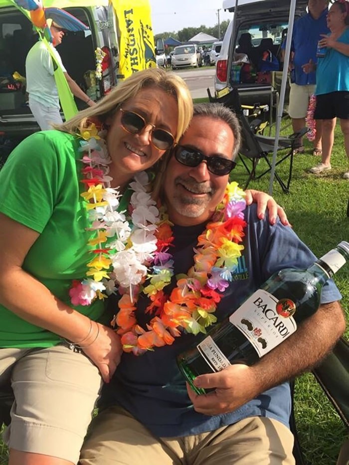 Happy parents wearing colorful leis and sunglasses, sharing a fun and wholesome moment outdoors at a casual gathering.