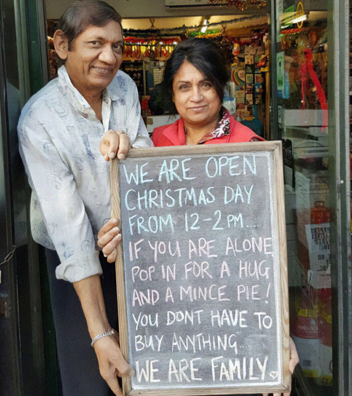 Two people holding a chalkboard sign offering hugs and mince pies on Christmas Day, spreading wholesome kindness.