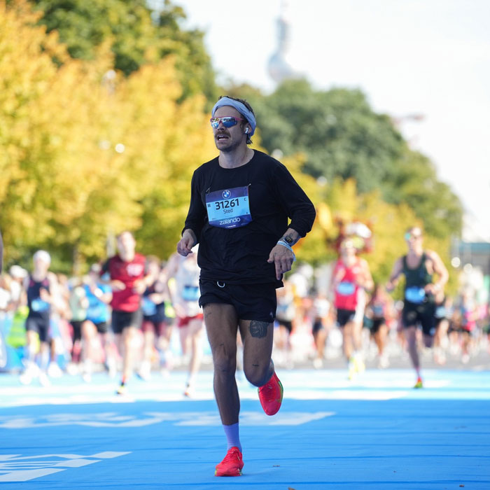 Runner in black outfit and red shoes competing in Berlin Marathon, showcasing impressive speed during the race.