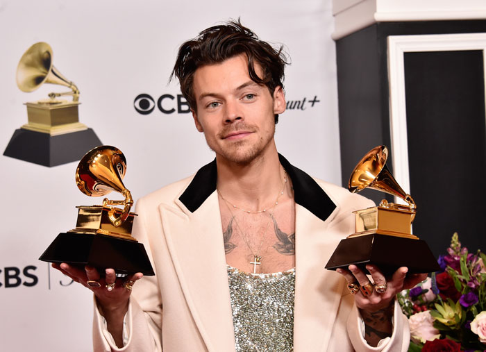 Harry Styles holding two Grammy awards, recognized for secretly running Berlin marathon with impressive speed.